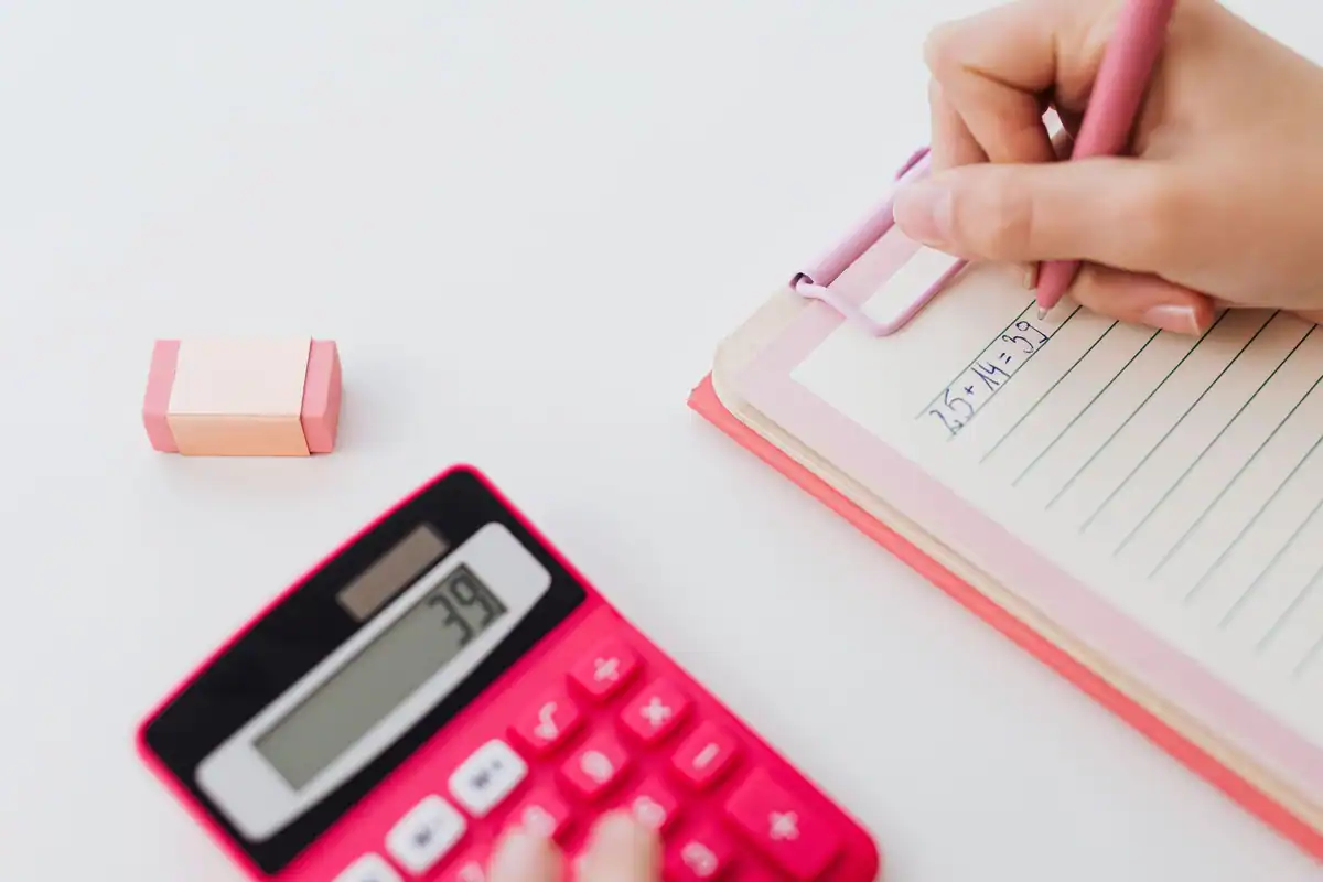 Mâini care folosesc un calculator și notează calcule într-un caiet