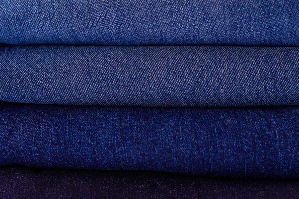 Țesături denim împăturite în teanc, în diferite nuanțe de albastru