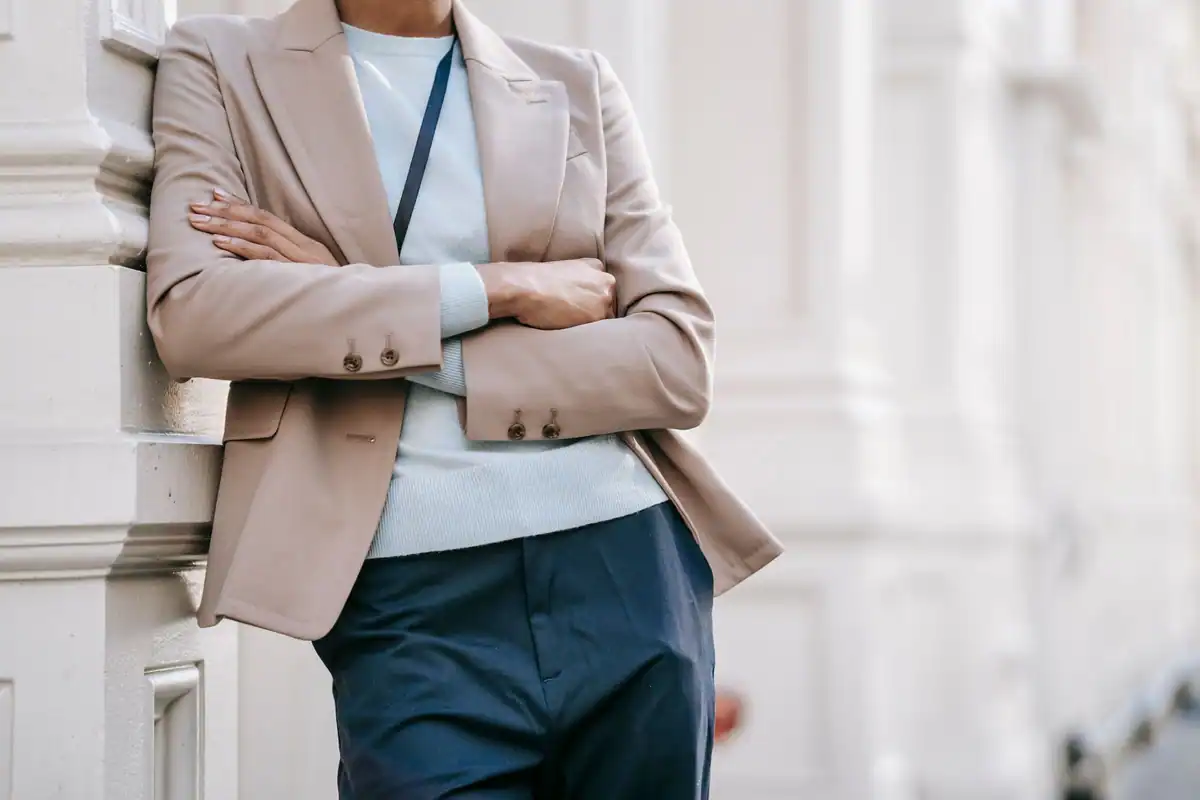 Femeie într-o ținută smart casual, cu brațele încrucișate lângă o clădire elegantă