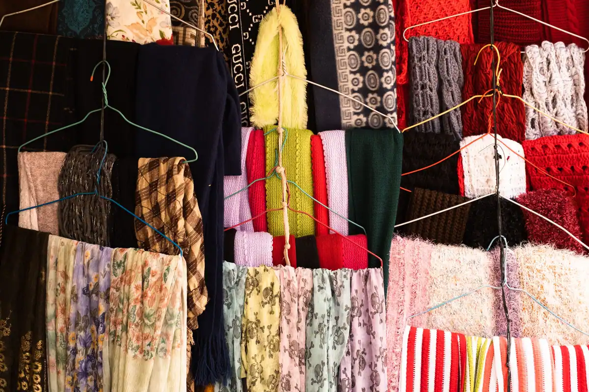 Eșarfe colorate din diverse materiale atârnate pe umerașe de sârmă