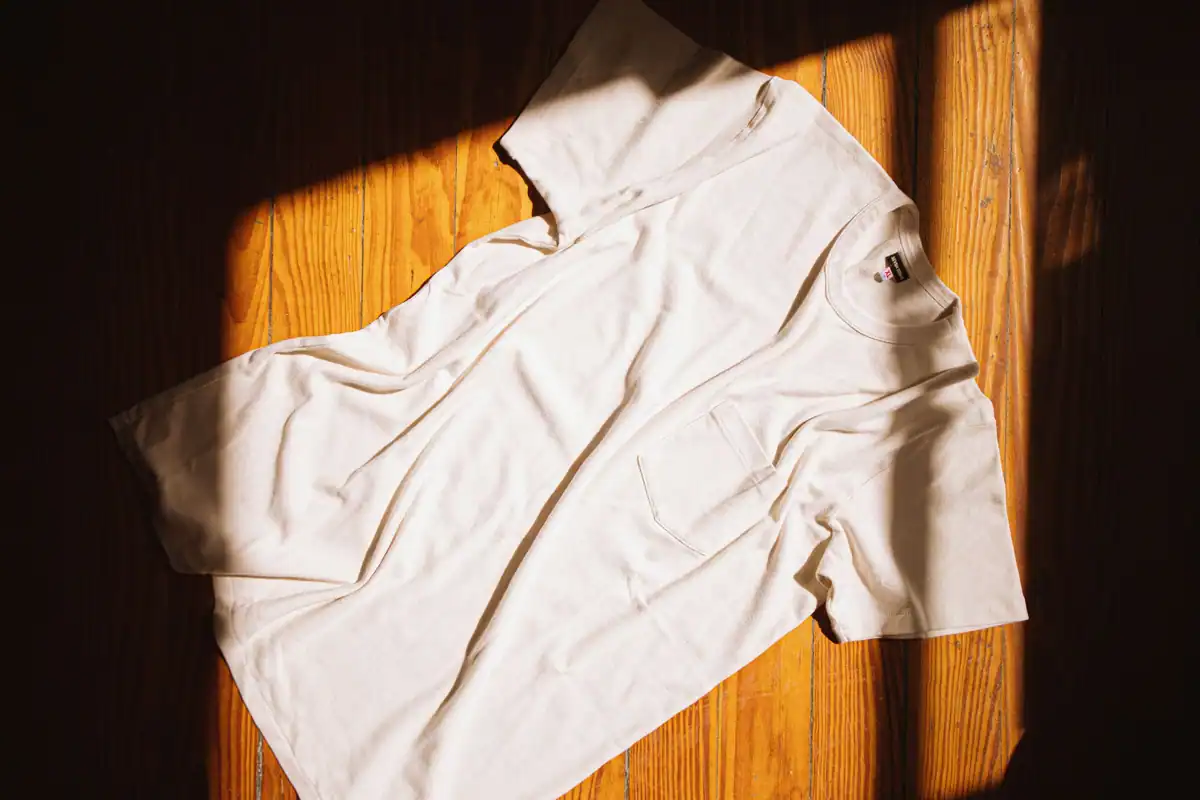 Tricou alb simplu întins pe o podea de lemn în lumina caldă a soarelui