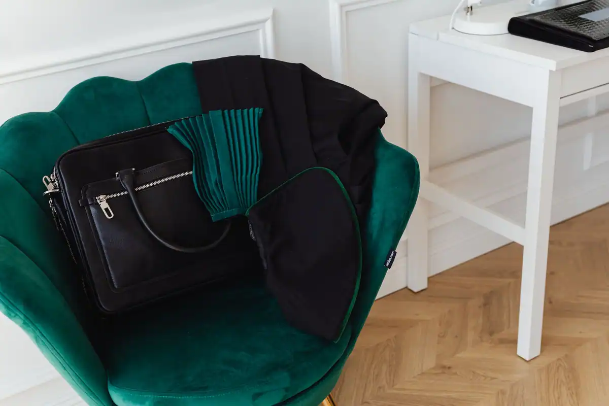 Geantă neagră de mână așezată pe un fotoliu verde într-un interior minimalist