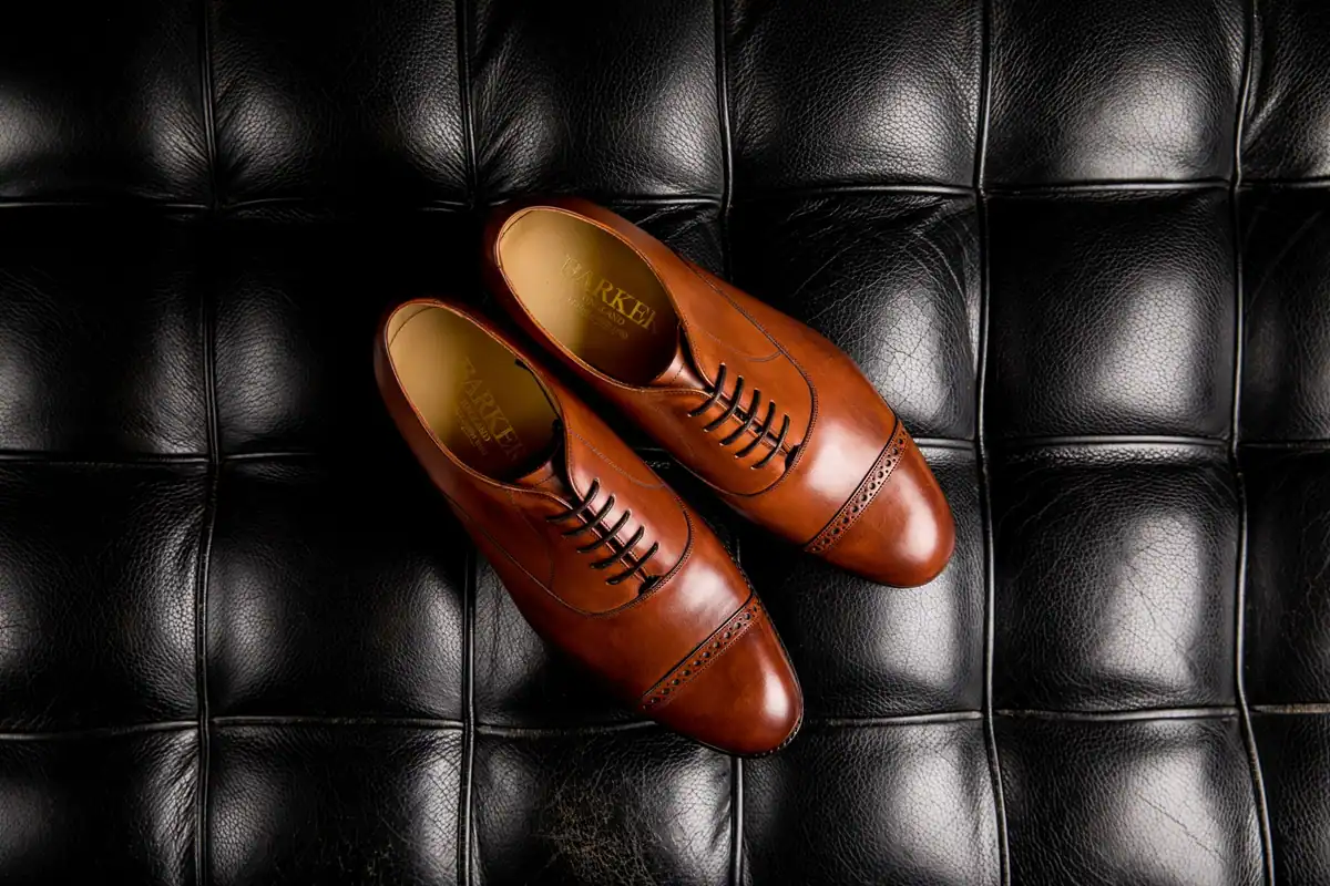 Pantofi oxford din piele maro așezați pe o suprafață matlasată neagră