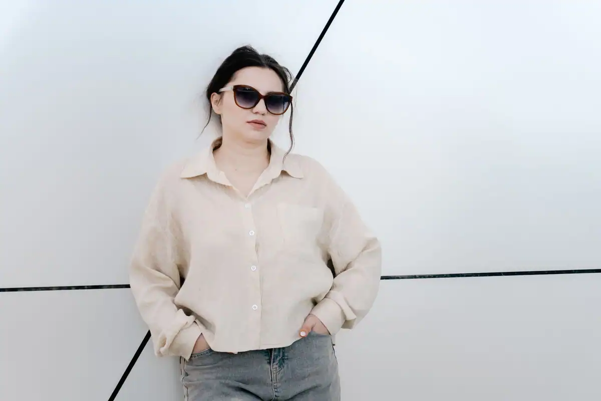 Femeie cu ochelari de soare sprijinită de un perete cu forme geometrice